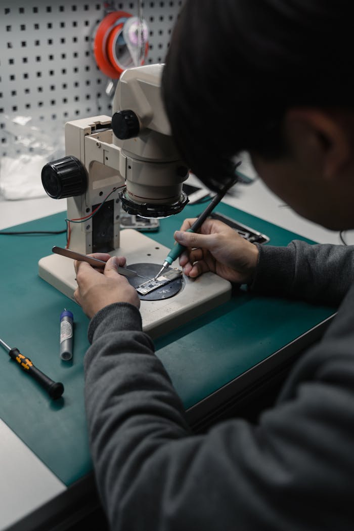 Focused technician soldering microchip under microscope in electronics lab.